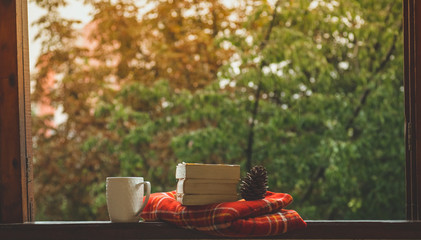 Cozy autumn still life: cup of hot coffee and opened book on vintage windowsill and rain outside. Autumn. Apartment. Rain 