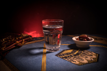 Water and dates. Iftar is the evening meal. View of decoration Ramadan Kareem holiday on carpet. Festive greeting card, invitation for Muslim holy month Ramadan Kareem. Dark background