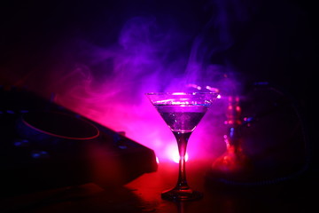 Glass with martini with olive inside on dj controller in night club. Dj Console with club drink at music party in nightclub with disco lights.