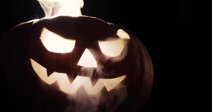 Scary carved halloween pumpkin in hot burning hell fire flames. The big helloween pumpkin has a mad face with glowing eyes and also a smoke in its mouth and teeth.