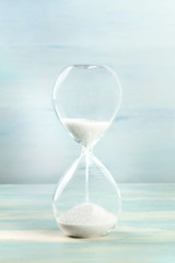 A side view of an hourglass with falling sand, on a teal background with copy space