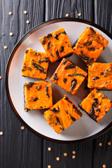 Halloween dessert cream Cheese Brownies consisting of a dark chocolate cake topped with a layer of orange cheesecake close-up. Vertical top view