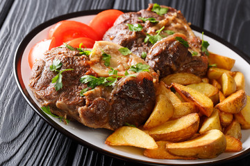 shank Ossobuko with a garnish of fried potato slices and fresh tomatoes close-up on a plate. horizontal