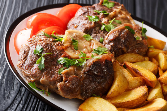 Delicious steak Ossobuco served fried potato slices and fresh tomatoes close-up on a plate. horizontal