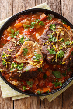 Italian veal steak Ossobuco alla Milanese with gremolata and spicy sauce closeup. Vertical top view