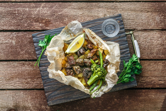 Lamb kleftiko, potato and vegetables served on wooden cutin board, rustic style