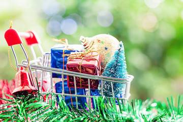 Full of Xmas decorative items in mini shopping cart or trolley against blurred natural green background for Christmas and New Year festival concept