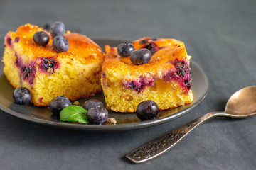 Two pieces of blueberry cake on a dark saucer.