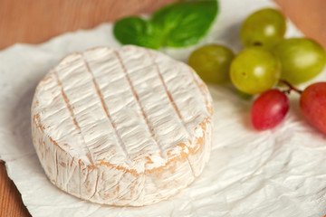 A soft ripened Camembert cheese and grapes on a white background
