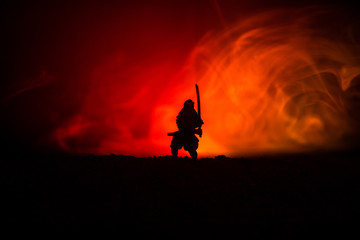 Fighter with a sword silhouette a sky ninja. Samurai on top of mountain with dark toned foggy background.