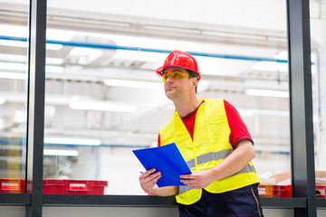 Factory supervisor in yellow reflective west with red helmet. Factory engineer holding blue folder with documents