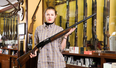 Fototapeta na wymiar Smiling female in hunting shop with rifle