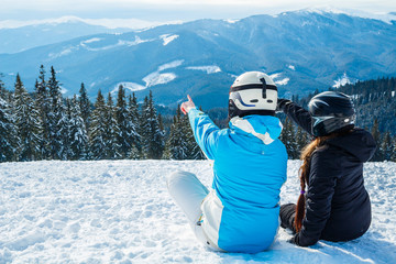 Fototapeta na wymiar two girls sitting on the snow looking at the mountains
