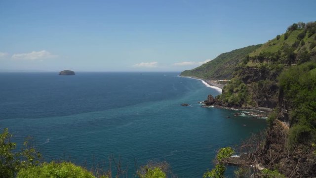Rocky coast with high cliffs, sea coast, ocean, mountains, sea, beach, sky, clouds. Bali, sea surf with breaking waves on the coast, Indonesia. Ocean with waves and rocky cliff. 4K video.