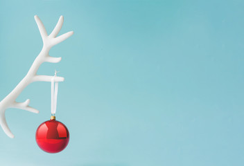 White reindeer antler with red Christmas bauble decoration on pastel blue background. New Year...