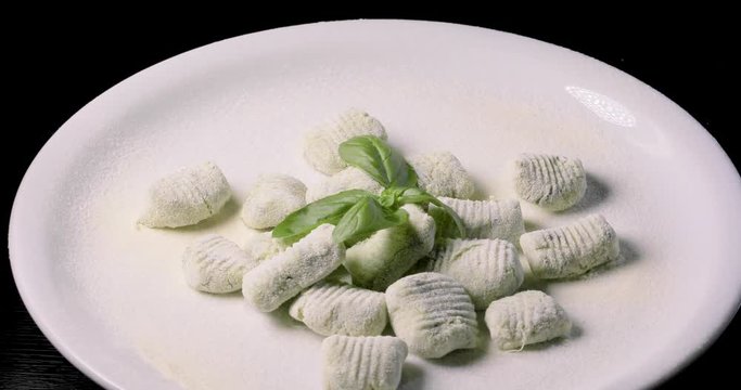 Gnocchi di patate verdi da cuocere con basilico fresco su un vassoio ruotante da esposizione. Cibo vegano.