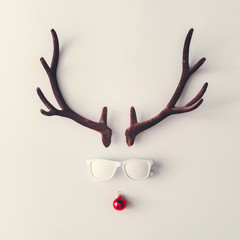 Santas reindeer made of antlers, white sunglasses and red New Year bauble decoration. Minimal...