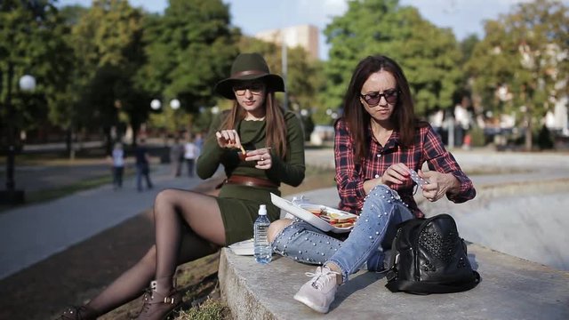 Two girls hipster in the Park eating sandwiches and talking