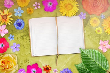 Beautiful flower frame with notebook in center on yellow decorative plaster background. Floral composition of spring or summer flowers.