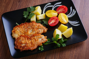 Steak of pork with potatoes and tomatoes on a figured black plate