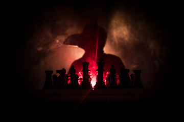 Man playing chess. Scary blurred silhouette of a person at the chessboard with chess figures. Dark toned foggy background.