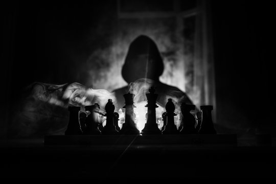 Man playing chess. Scary blurred silhouette of a person at the chessboard with chess figures. Dark toned foggy background.