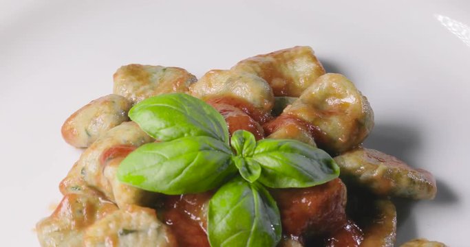 Gnocchi di patate fatti in casa verdi con salsa al pomodoro e basilico fresco su un piatto da esposizione per un ristorante.