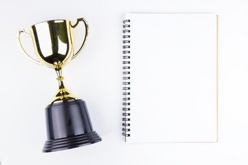 Top view of Blank notebook white paper and Golden trophy isolated on white background with space for your message.Concept winner.