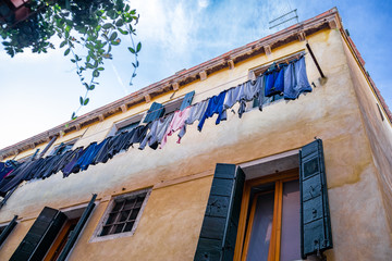 Upward view of clothes drying on clothes line with sky, windows & shutters, in Venice, Italy.