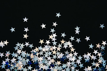 Shiny stars of foil on black background. Festive confetti.
