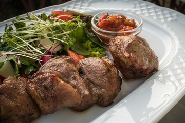 shish kebab closeup with vegetables and sauce on a plate, blurred background with vignette