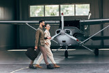 side view of man carrying bag and walking with stylish girlfriend near hangar with plane