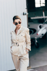 Obraz premium young beautiful woman in sunglasses and jacket posing with hands in pockets near airplane