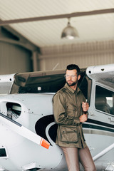 young stylish man in green jacket and eyeglasses looking away near airplane