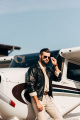 confident male pilot in leather jacket and sunglasses posing near airplane © LIGHTFIELD STUDIOS