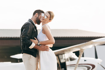 selective focus of fashionable man in leather jacket embracing attractive girlfriend near plane