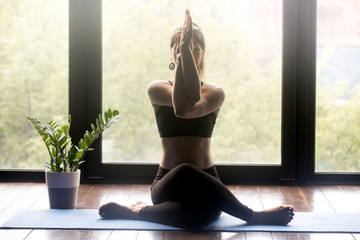 Young sporty woman practicing yoga, doing Gomukasana exercise, Cow Face pose, working out, wearing sportswear, grey pants and top, indoor full length, yoga studio