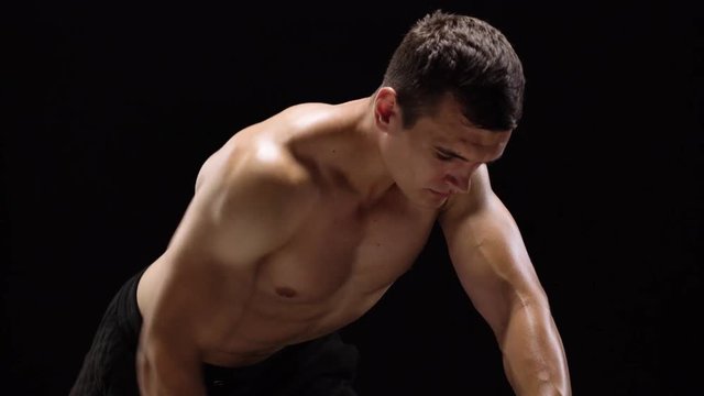 Man flexes his hands with dumbbells, training his back on a black background in the studio