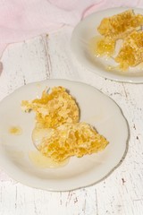 two white dessert plates with pieces of honeycomb on a light wooden background
