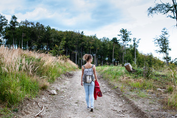 Beautiful woman smiling at path in a forest during hiking on a hill during sunrise on summer