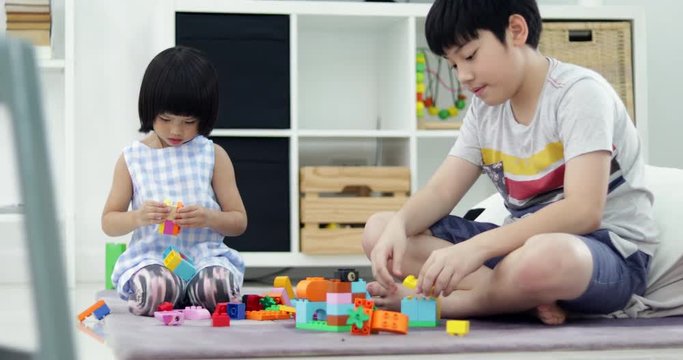 Asian brother and sister playing plastic block together at home with smile face.