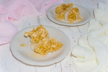 two white dessert plates with pieces of honeycomb on a light wooden background
