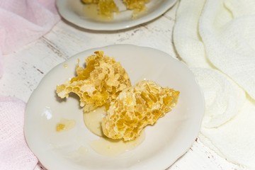 two white dessert plates with pieces of honeycomb on a light wooden background
