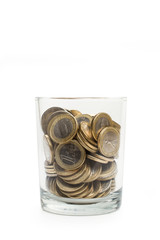 Monedas dentro de un vaso hucha de cristal sobre fondo blanco aislado. Vista de frente y de cerca. Concepto ahorro. Copy space. Formato vertical - obrazy, fototapety, plakaty