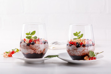 Chia pudding with fresh currant berries in glass on white table.