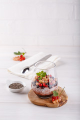 Chia pudding with fresh currant berries in glass on white table.