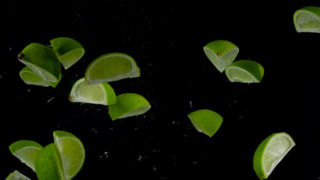 Lime pieces fall and float in water, black background
