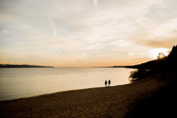 Two lovers stroll along the river at sunset.