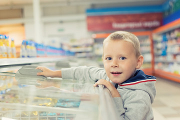 Obraz premium A child, a small boy 5-7 years old, opens a cold store in a supermarket.