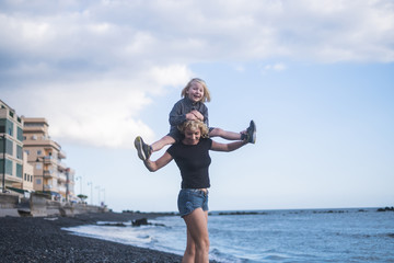 happy woman mother walk with his son long hair blonde walking at the beach carrying him on the back. beautiful people enjoying lifestyle and life outoor with the nature. vacation and lifestyle concept